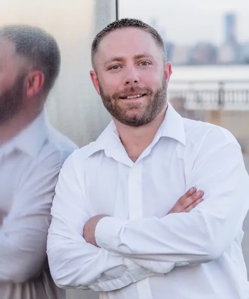 A man in white shirt and beard with arms crossed.